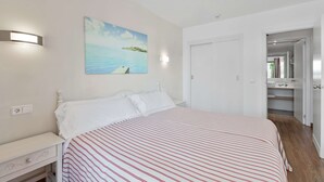 Een slaapkamer met een bed, nachtkastje, een wandlamp en een schilderij van een strand.