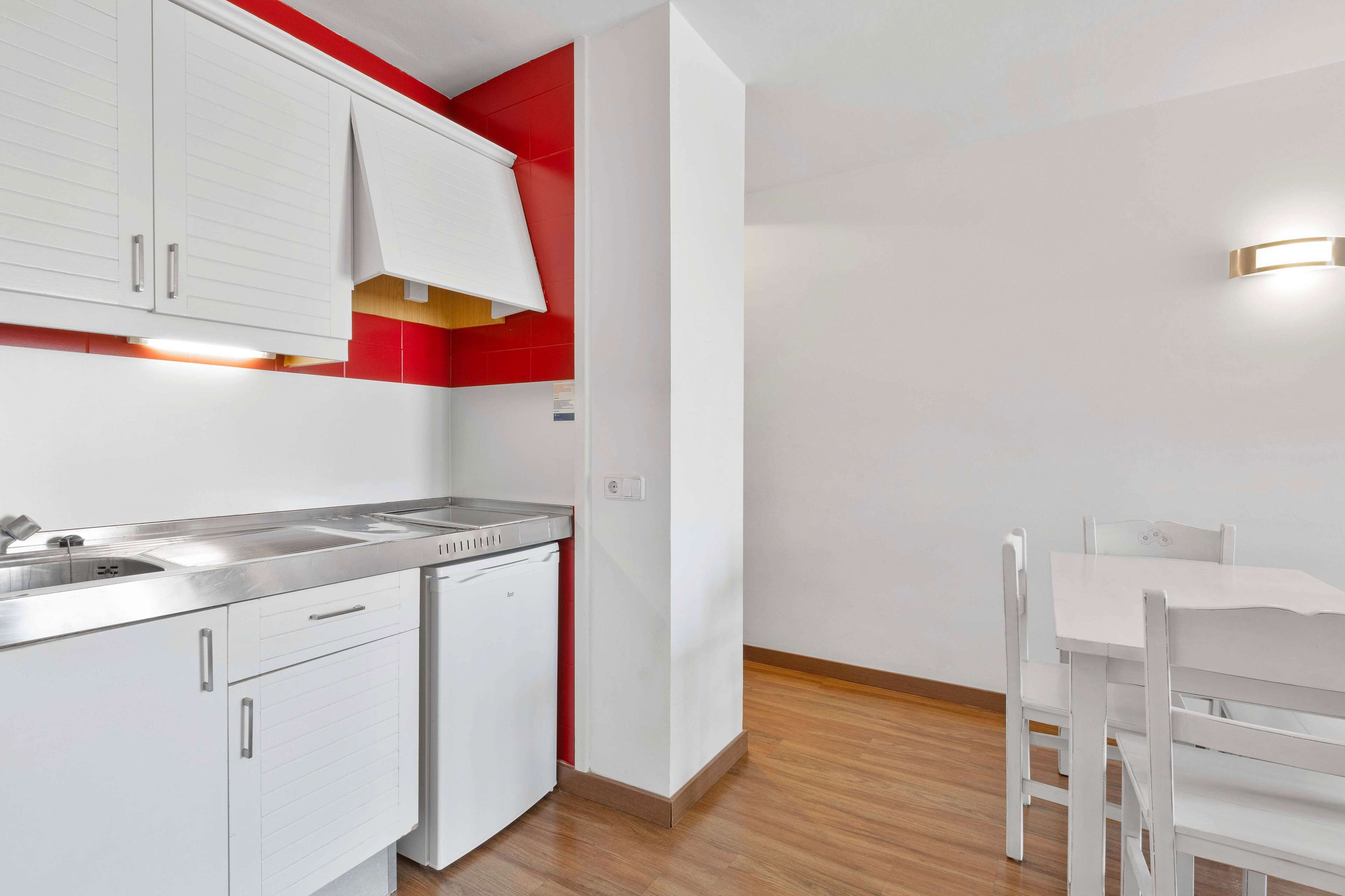 Une cuisine moderne avec des meubles blancs, un évier en acier inoxydable et un mur d’accent rouge.