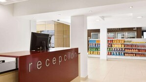 Zona de recepción con un mostrador que dice “recepción” y un supermercado al fondo.