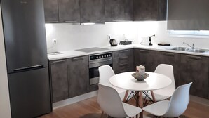 A modern kitchen with dark grey cabinets, a stainless steel refrigerator, a built-in oven, and a white dining table with four chairs. - Διαμέρισμα  (Αθηνα)