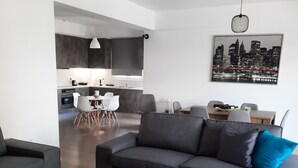 A modern living room with a grey sofa, a coffee table, and a dining area with a table and chairs. - Διαμέρισμα  (Αθηνα)
