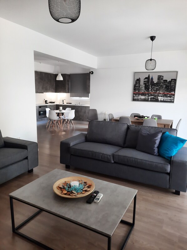 Ein modernes Wohnzimmer mit einem grauen Sofa, einem Couchtisch und einem Essbereich mit Tisch und Stühlen.
