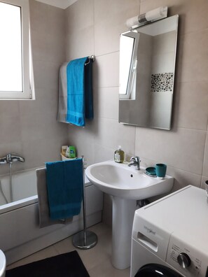 Ein Badezimmer mit einem weißen Waschbecken, einem Spiegel, einem blauen Handtuch, einer weißen Waschmaschine und einer Badewanne.