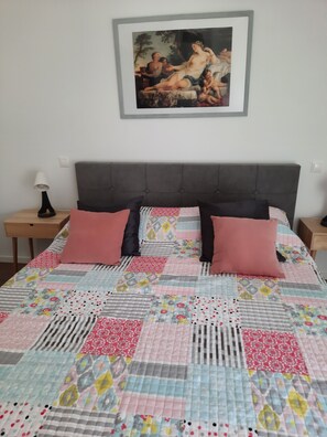 Ein Schlafzimmer mit einem großen Bett, einem grau gepolsterten Kopfteil und einem darüber hängenden Gemälde.
