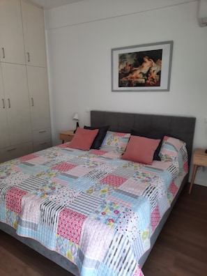 Ein Schlafzimmer mit einem großen Bett, einem Nachttisch, einem Kleiderschrank und einem gerahmten Bild an der Wand.