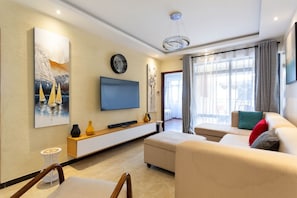 A modern living room with a flat-screen TV, a sofa, a coffee table, and a dining area with chairs.