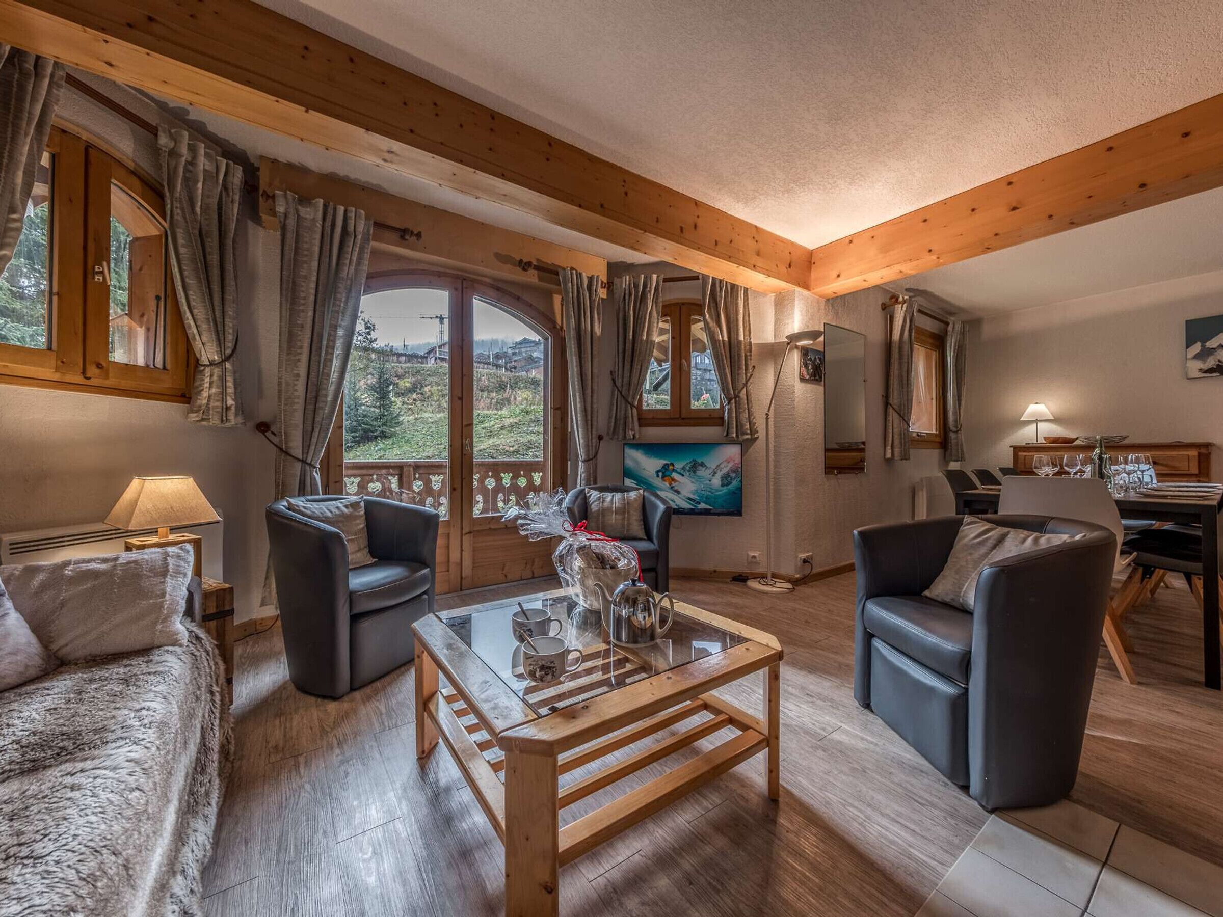 Ein gemütliches Wohnzimmer mit Holzbalken, einem Glastisch und einem schönen Ausblick durch große Fenster.