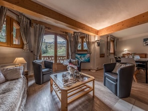 A cozy living room with wooden beams, a glass coffee table, and a scenic view through large windows.
