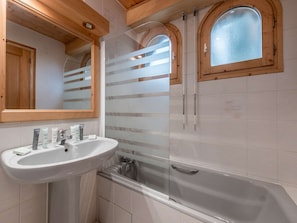 A bathroom with a white sink, a mirror, a shower with frosted glass doors, and wooden beams on the ceiling.