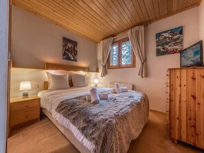 A bedroom with a wooden ceiling, a bed with a fur throw, two nightstands with lamps, a wooden dresser, and two framed pictures on the wall. - "Duplex Cosy 90m² à Courchevel 1850 - 8 Pers - Pieds des Pistes - Cheminée & Double Garage" (Courchevel 1850)