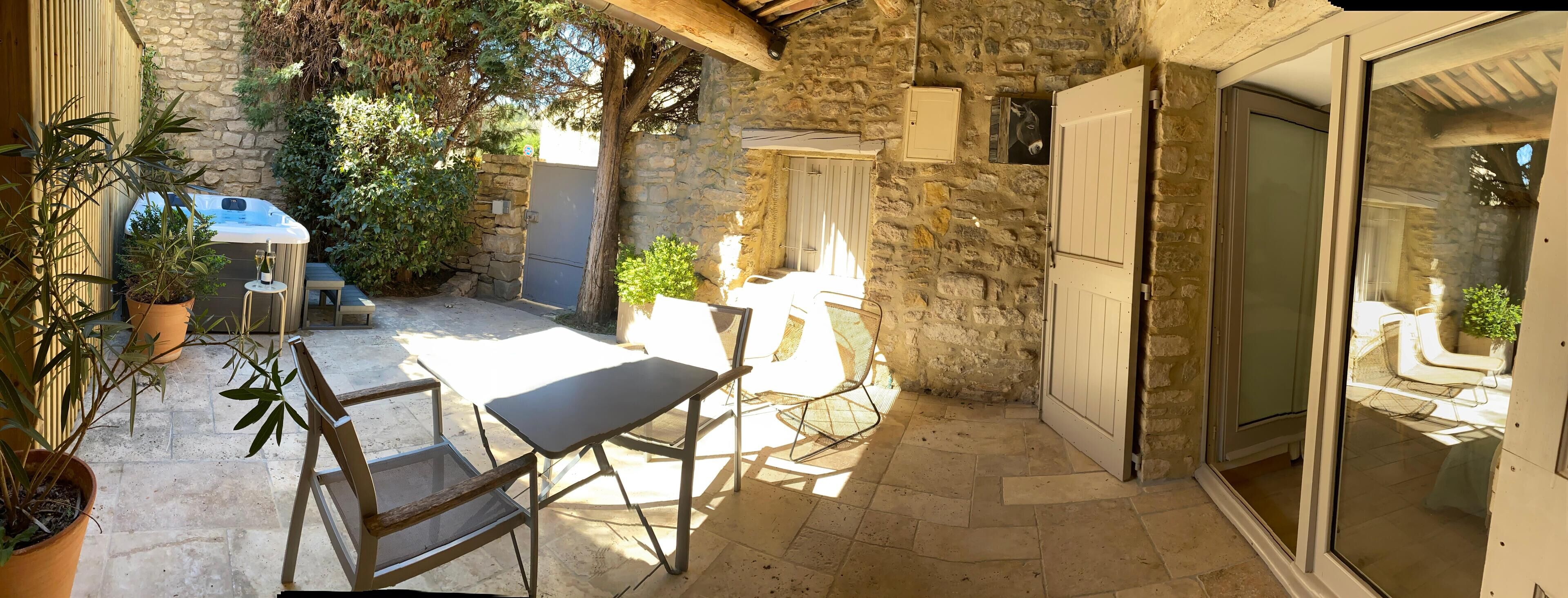 Eine Terrasse mit Steinmauern, einem Whirlpool, Sitzmöbeln im Freien und einer Glasdoor, die zu einem überdachten Bereich führt.