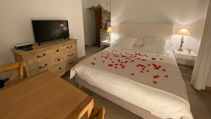 A hotel room with a bed, a TV on a wooden dresser, a desk, and a nightstand with a lamp. - CHAMBRE GRAND CONFORT COQUET with PRIVATE JACUZZI (Martignargues)