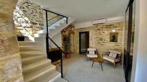 Un escalier mène à un salon aux murs de pierre, aménagé avec deux canapés et un téléviseur.