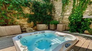 Un bain à remous installé à l’extérieur, avec des murs en pierre et de la verdure tout autour.
