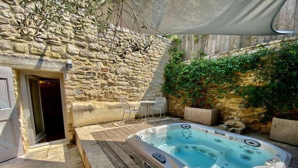 Un bain à remous dans un espace extérieur entouré de murs en pierre, avec une terrasse en bois, une petite table et une chaise.
