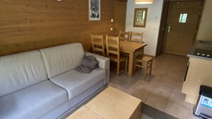 Un saló modern amb un sofà, una taula de centre de fusta, una taula de dinar amb cadires, i una zona de cuina amb fogons.