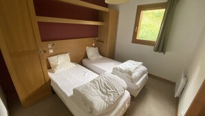 Un dormitori amb dos llits, ambres a les capçaleres de fusta, una finestra amb cortines i una làmpada al sostre.