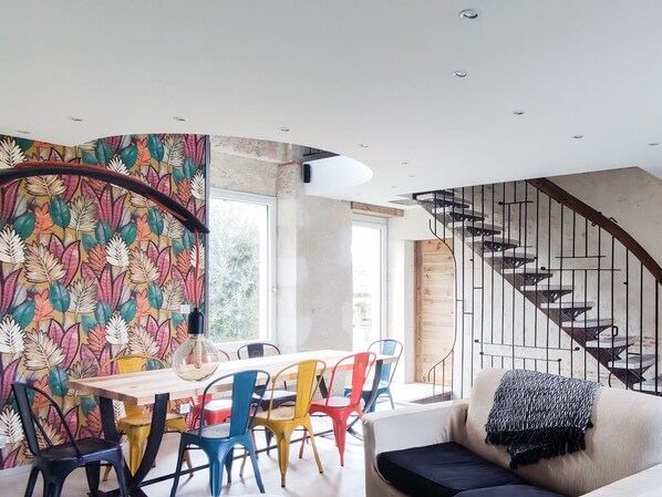 A modern interior with a dining area, colorful chairs, a sofa, and a spiral staircase.