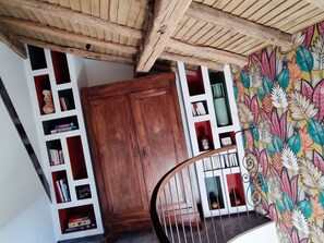 Eine Holztreppe mit einer Wendeltreppe, ein Bücherregal mit unterschiedlichen Büchern und eine Wand mit einem farbenfrohen Blattmuster.