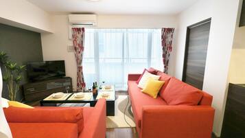Una sala de estar moderna con un sofá rojo, una televisión y un comedor con una mesa lista para dos.