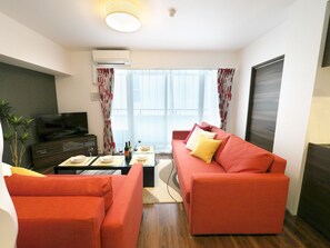 A modern living room with a red sofa, a television, and a dining area with a table set for two. - Kicon-hotels Marunouchi (Nagoya)