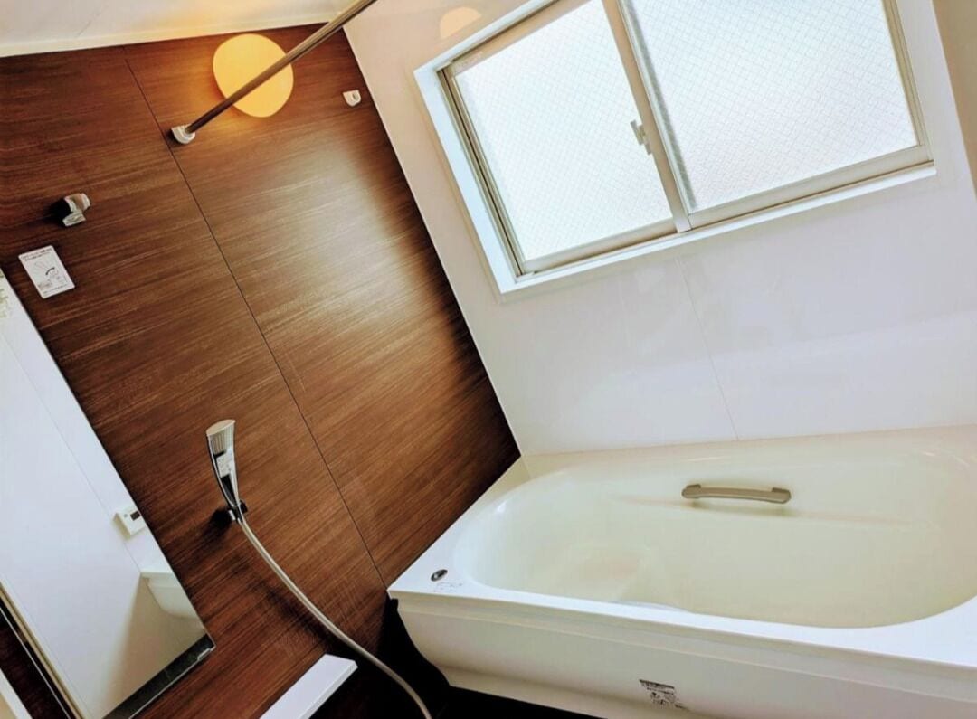 A modern bathroom with a bathtub, wooden flooring, a window, and a towel rack.