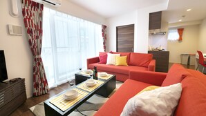 A modern living room with a red sofa, a dining table set with plates and wine glasses, and a large window with curtains. - Kicon-hotels Marunouchi (Nagoya)