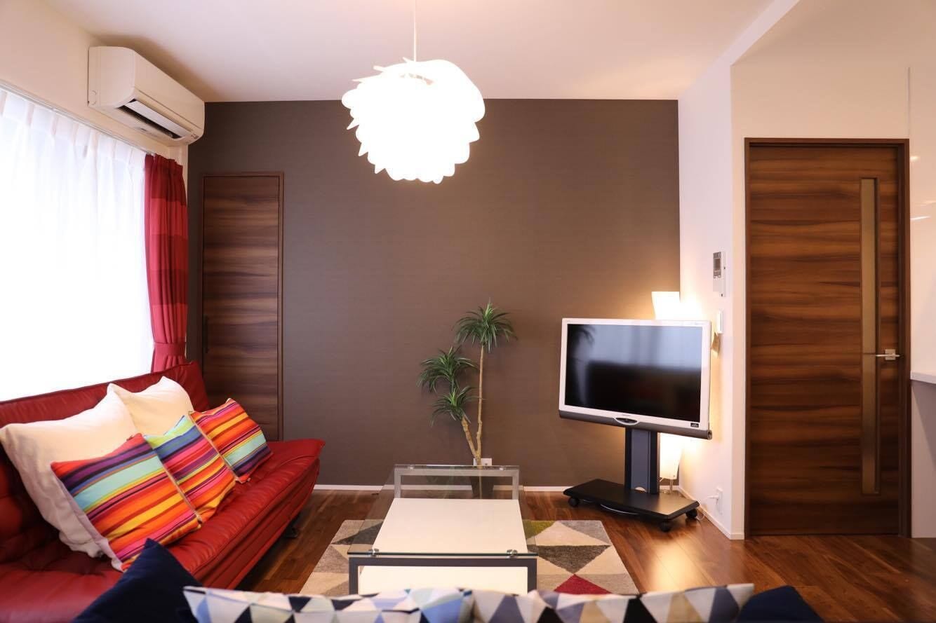 Un salon moderne avec un canapé rouge, un téléviseur à écran plat, une petite table et une plante décorative.