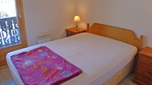 A bedroom with a bed, a nightstand with a lamp, a wooden headboard, and a window with a view. - Charming Apartment in Samoëns with Balcony and Parking, Sleeps 6 (Samoëns)