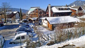 A snowy village with a row of parked cars, wooden buildings, and a mountain in the background. - Charming Apartment in Samoëns with Balcony and Parking, Sleeps 6 (Samoëns)