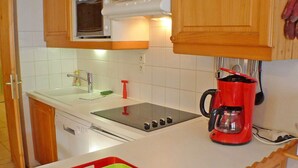 A compact kitchen with a microwave, stove, sink, and a red coffee maker. - Charming Apartment in Samoëns with Balcony and Parking, Sleeps 6 (Samoëns)
