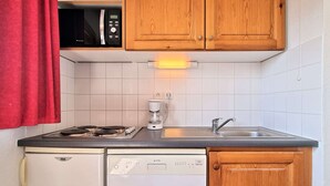 A compact kitchen with a dishwasher, a coffee maker, a microwave, and wooden cabinets.