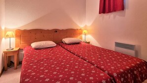 A bedroom with two beds, each with a red floral bedspread, wooden headboard, and two bedside lamps.