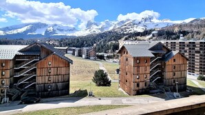A view of wooden cabins with a mountain backdrop, a clear sky, and a snow-covered peak in the distance.