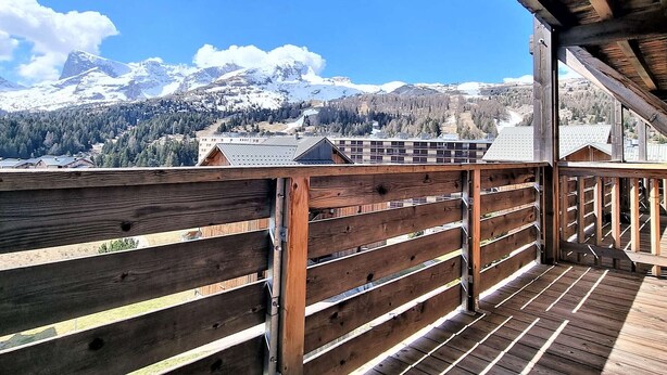 A wooden deck with a view of snow-capped mountains and a forested valley.