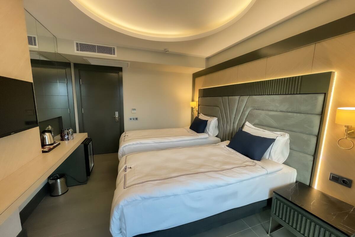 Ein Hotelzimmer mit zwei Betten, einem Schreibtisch, einem Spiegel und einem kleinen Tisch mit einer Lampe.