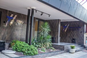 A modern building entrance with a prominent 'TURKAY' sign, a glass door, and a small garden area with plants.