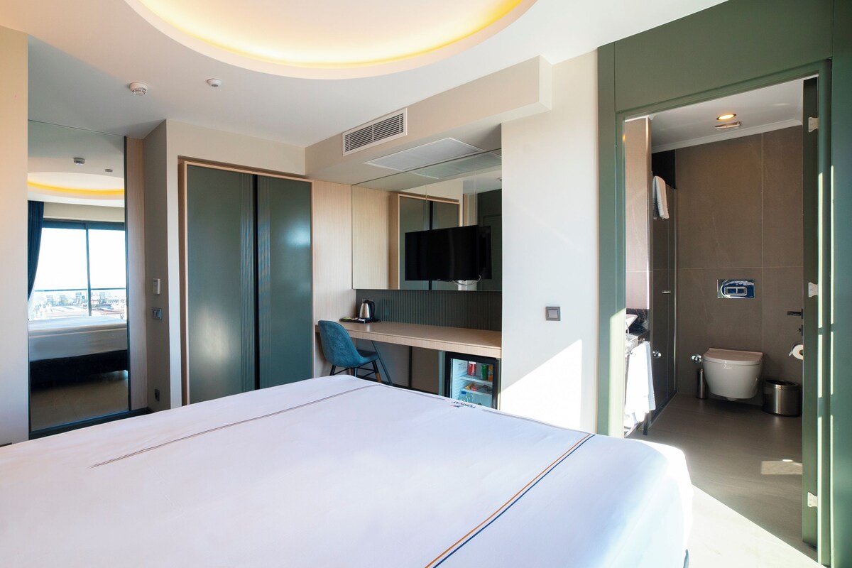 Una habitación de hotel moderna con una cama grande, un escritorio, una silla, un televisor y un baño.