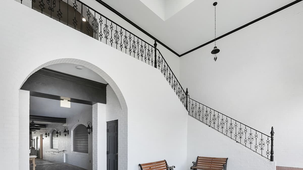 Una escalera con barandillas de metal ornamentadas, un banco de madera y un acceso a otra habitación.
