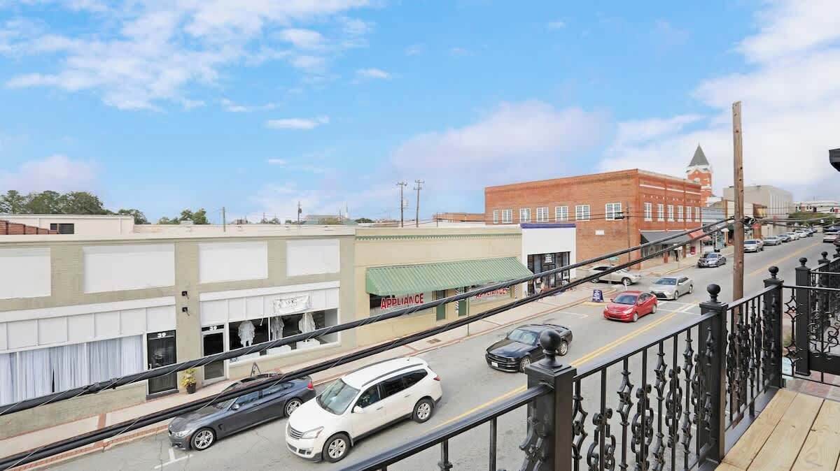 A street view with buildings, a red brick building with a tower, and a white car on the road.