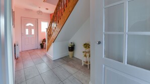 A spacious hallway with a wooden staircase, a white door, and a tiled floor. - 3 Bedroom Home. Home Working. Free Parking. Garden. Wigan (Wigan)