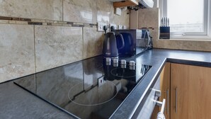 A modern kitchen with a black induction cooktop, a coffee maker, and a knife block. - 3 Bedroom Home. Home Working. Free Parking. Garden. Wigan (Wigan)