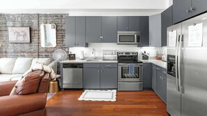 A modern kitchen with grey cabinets, stainless steel appliances, and a brick wall.