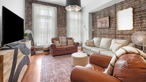 A modern living room with a brick wall, leather sofas, a coffee table, and a flat-screen TV.