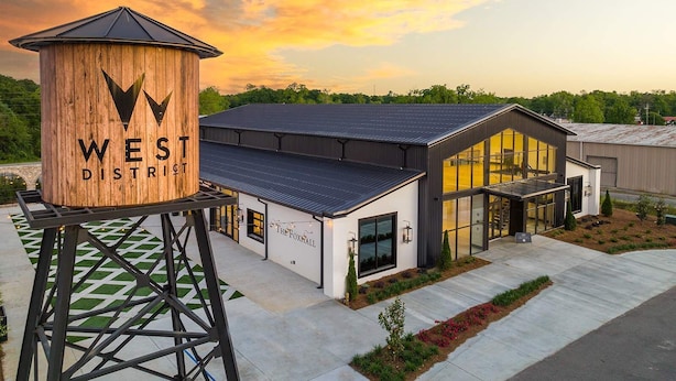 A modern building with a large wooden structure labeled "WEST DISTRICT" and a glass-fronted entrance. - Eagle Exec Loft In Downtown Statesboro (Statesboro)