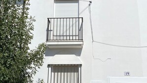Un bâtiment blanc avec une porte marron, un balcon doté de rampes en métal et une enseigne indiquant qu’il s’agit d’une maison de campagne.
