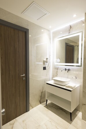 A modern bathroom with a wooden door, a white sink with a marble countertop, and a large mirror.