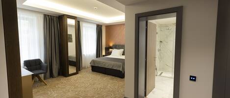 A hotel room with a bed, a desk, a chair, and a bathroom visible through an open door.