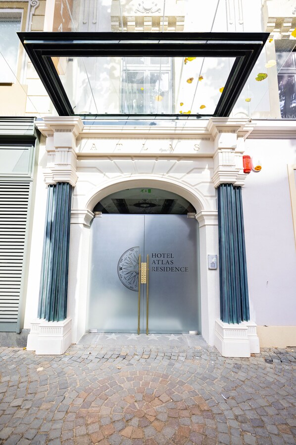 A hotel entrance with a large glass door, a star-studded pavement, and a clear view of the sky.