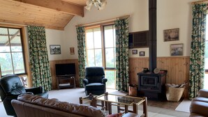 A cozy living room with a leather sofa, a black armchair, a glass coffee table, a television, and a wood-burning stove. - Mansfield Colonial Cabin with Stunning Views (Mansfield)